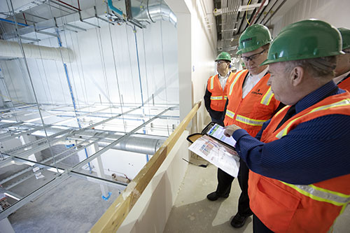 Photo of four workers wearing construction clothing and looking at paper on a clipboard.
