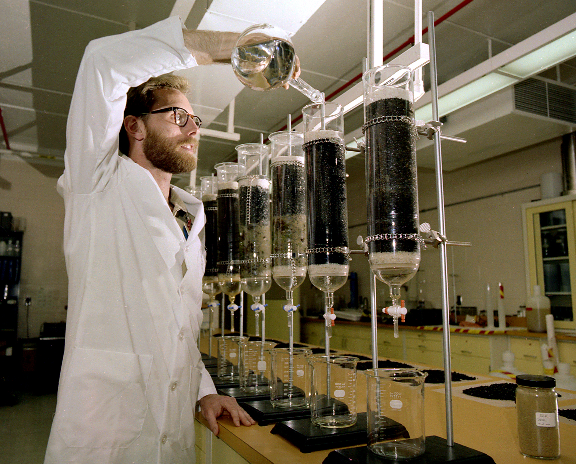 Scientist pouring liquid from a beaker into a titration system.